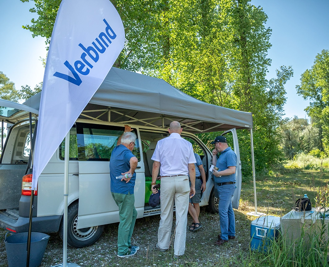 Individuals in casual attire conversing under a canopy with "Verbund" signage next to a van.